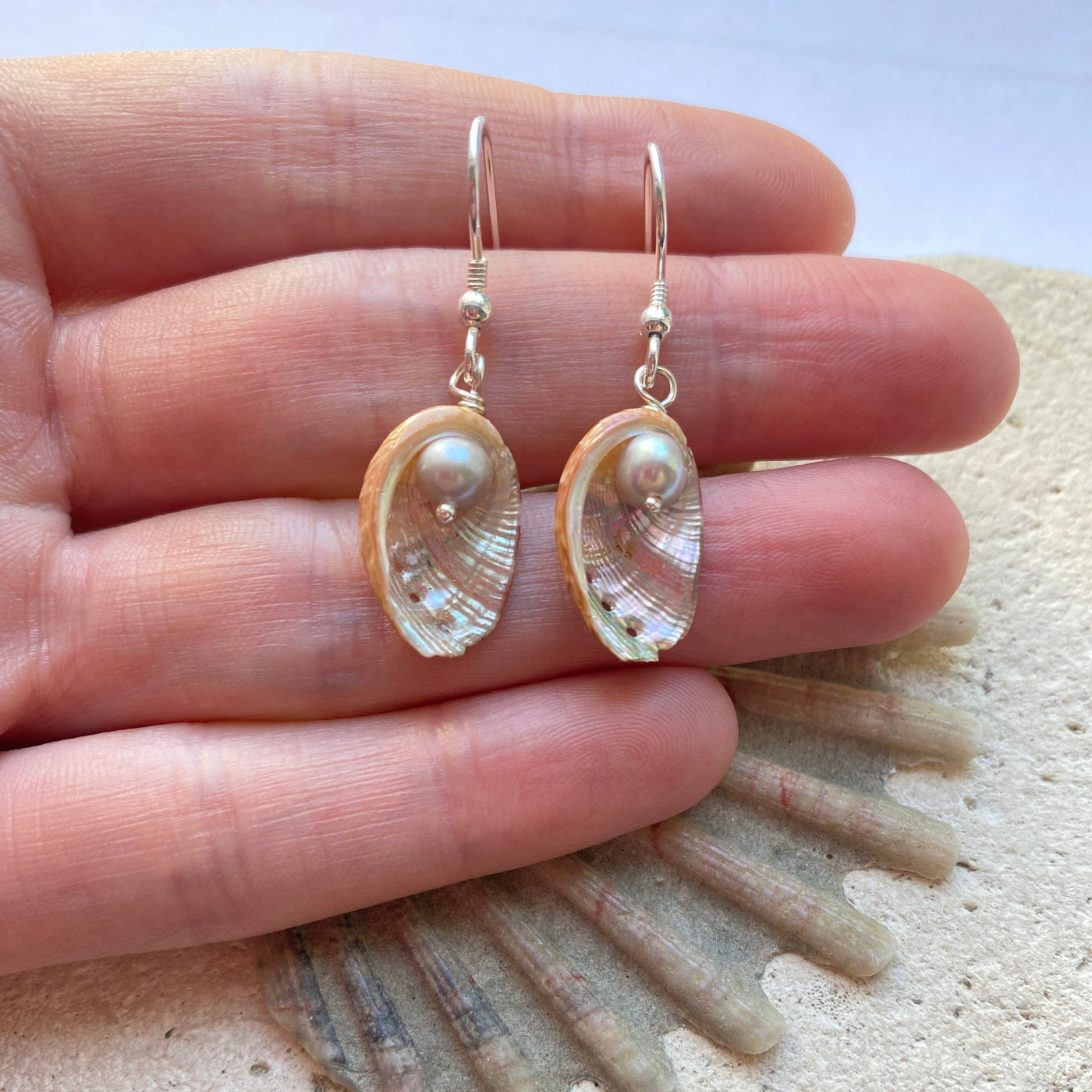 Guernsey Ormer shell hook earrings with grey freshwater pearl accent held in a hand 