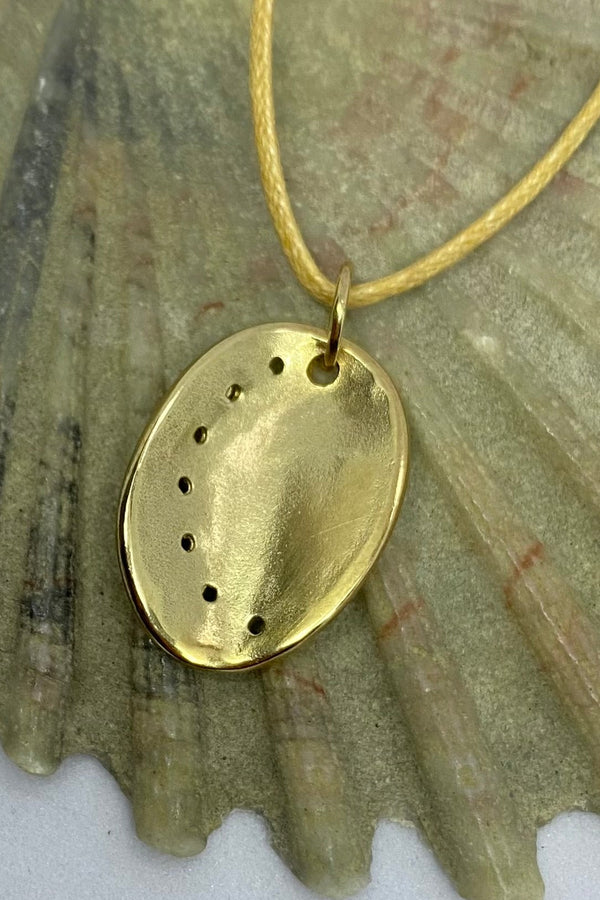 Guernsey ormer shell pendant in 9ct yellow gold on a cotton cord, laid on a seashell background