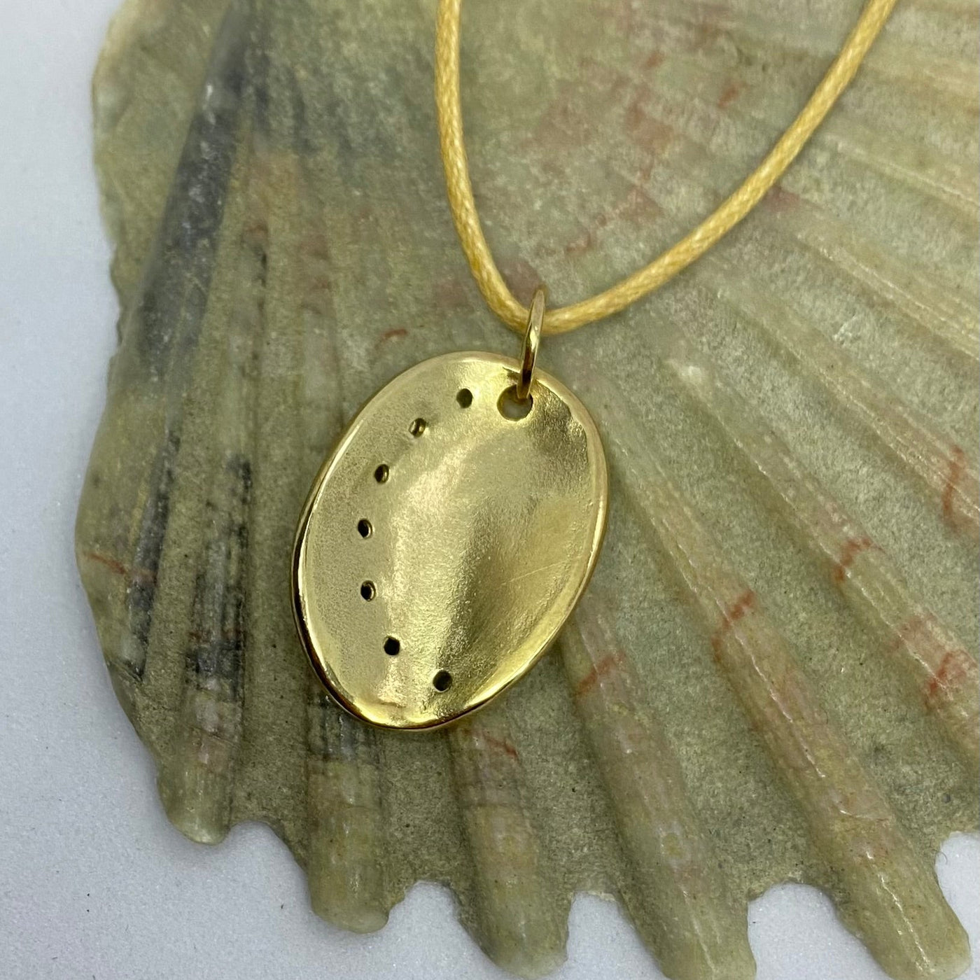 Guernsey ormer shell pendant in 9ct yellow gold on a cotton cord, laid on a seashell background