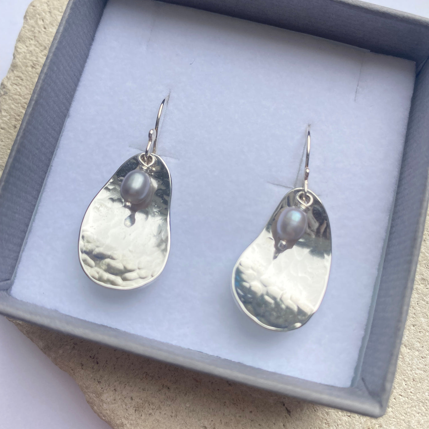 Silver potato peel pie inspired  teardrop shaped earrings in a gift box on a textured surface