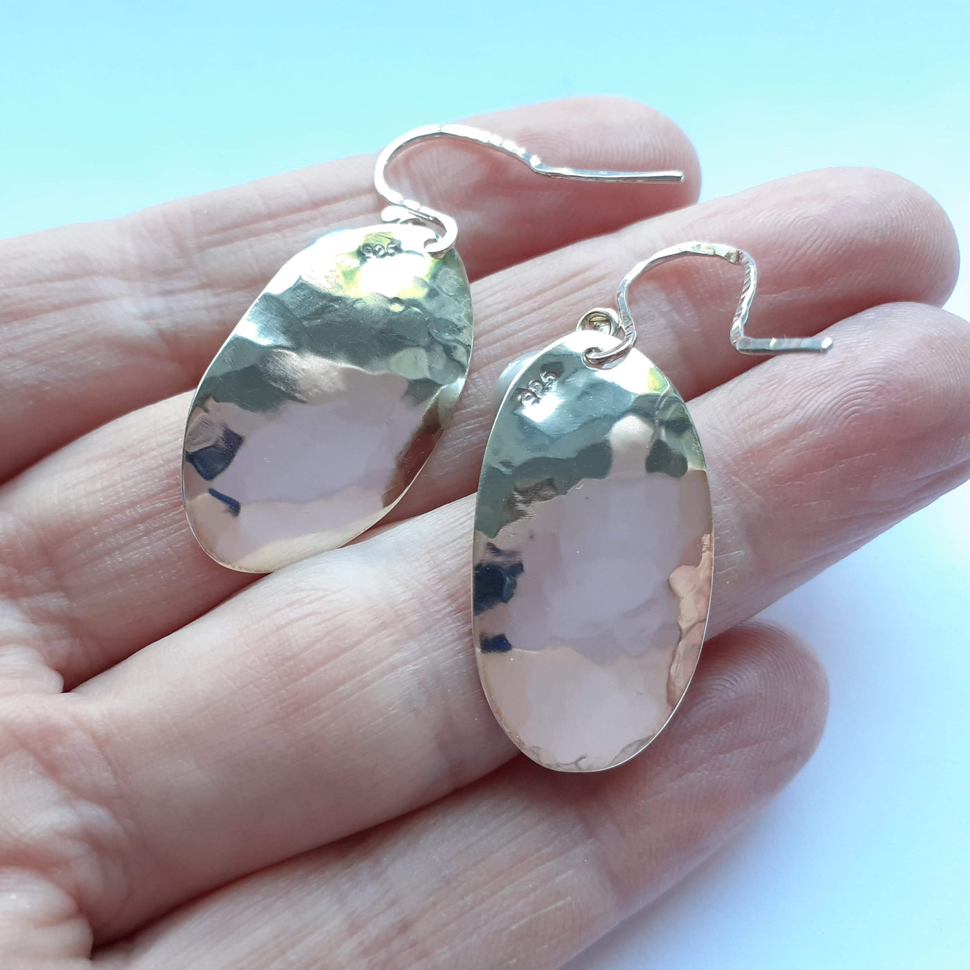 Reverse of a pair of potato peel pie earrings, showing the highly polished finish, displayed on the hands that made them. 