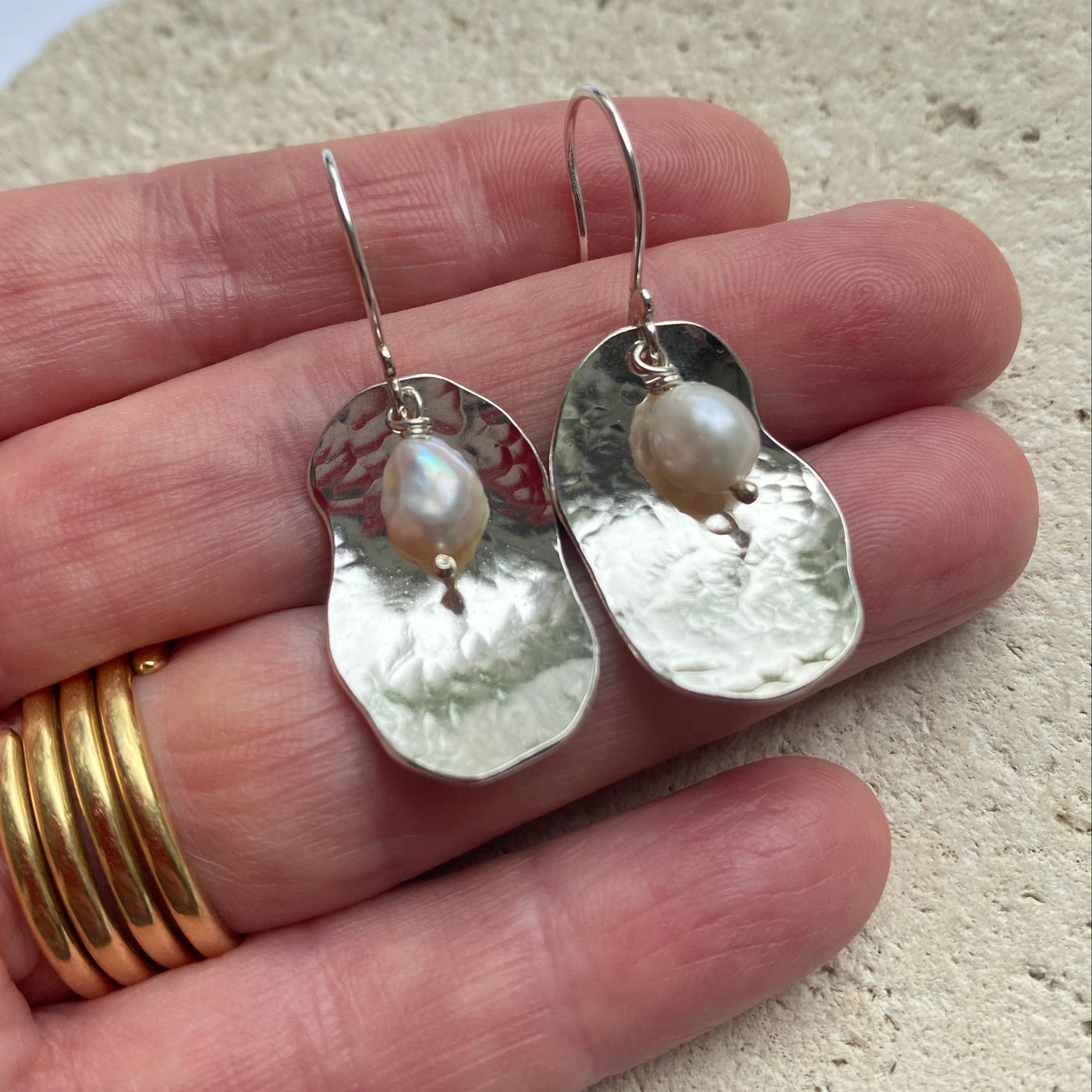 Silver potato peel pie earrings with freshwater pearls held in a hand against a neutral background