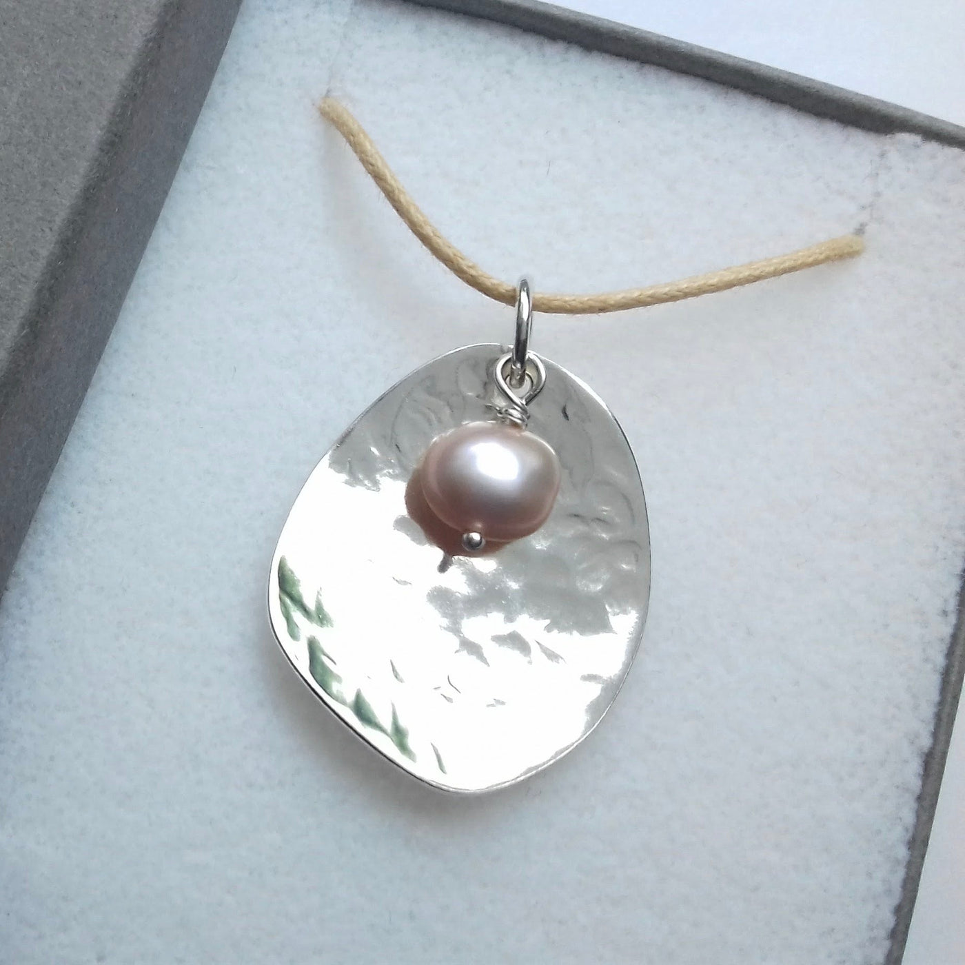 Silver potato peel pendant necklace with a pink pearl on a gray background