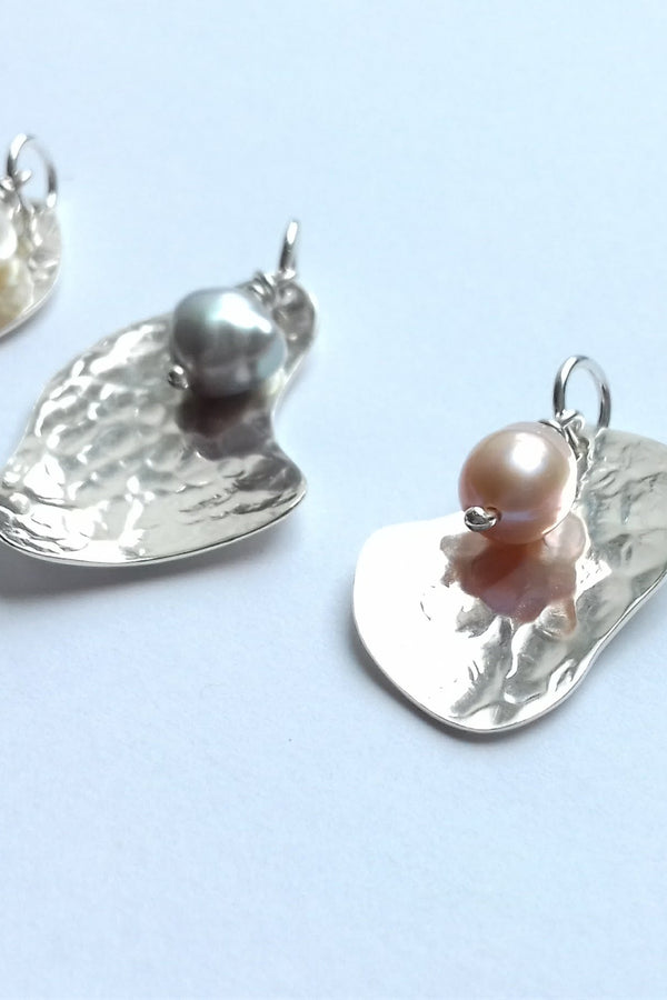 Silver potato peel-shaped pendants with pearls on a light blue background
