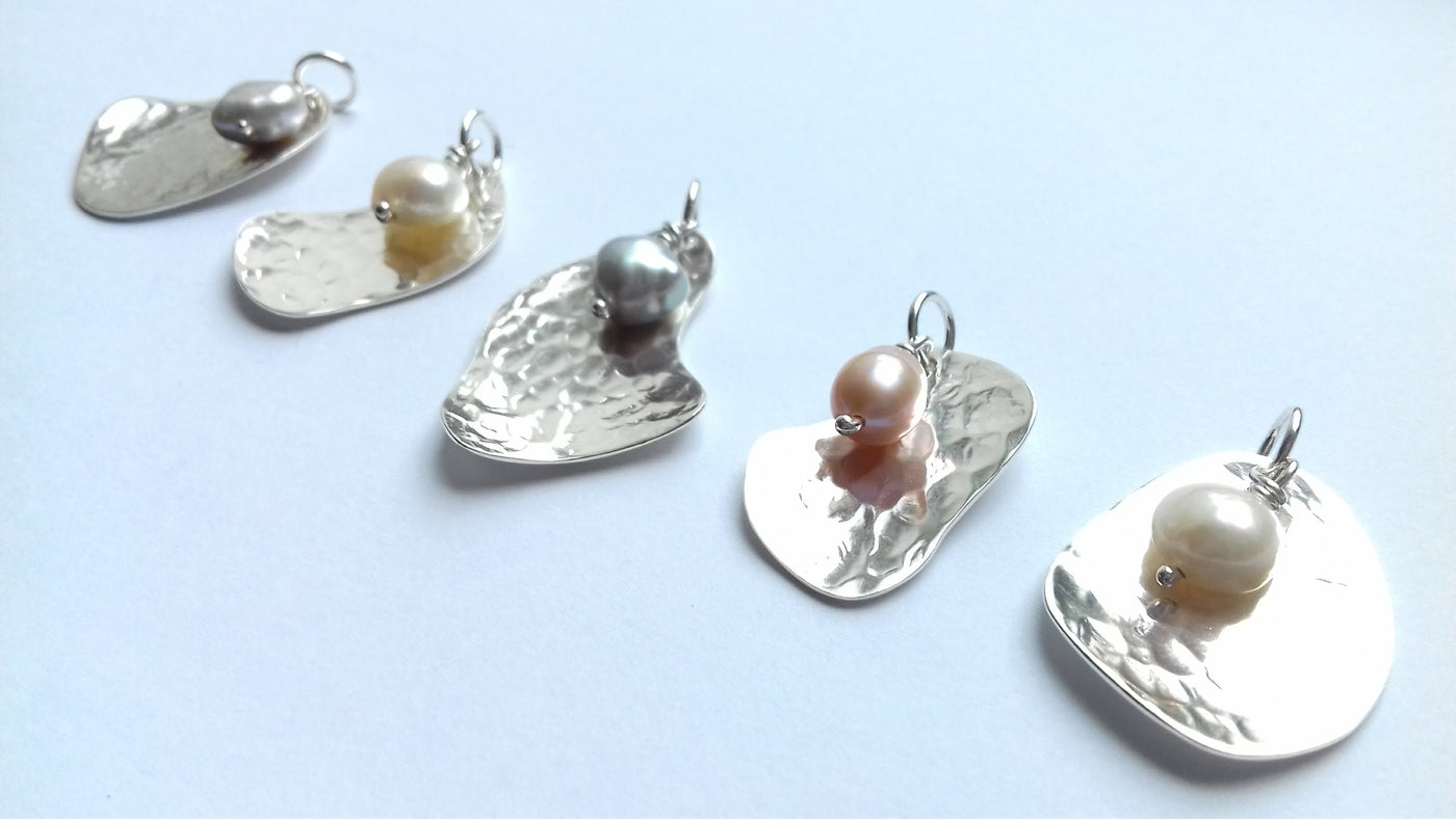 Silver potato peel shaped pendants with pearls on a light blue background