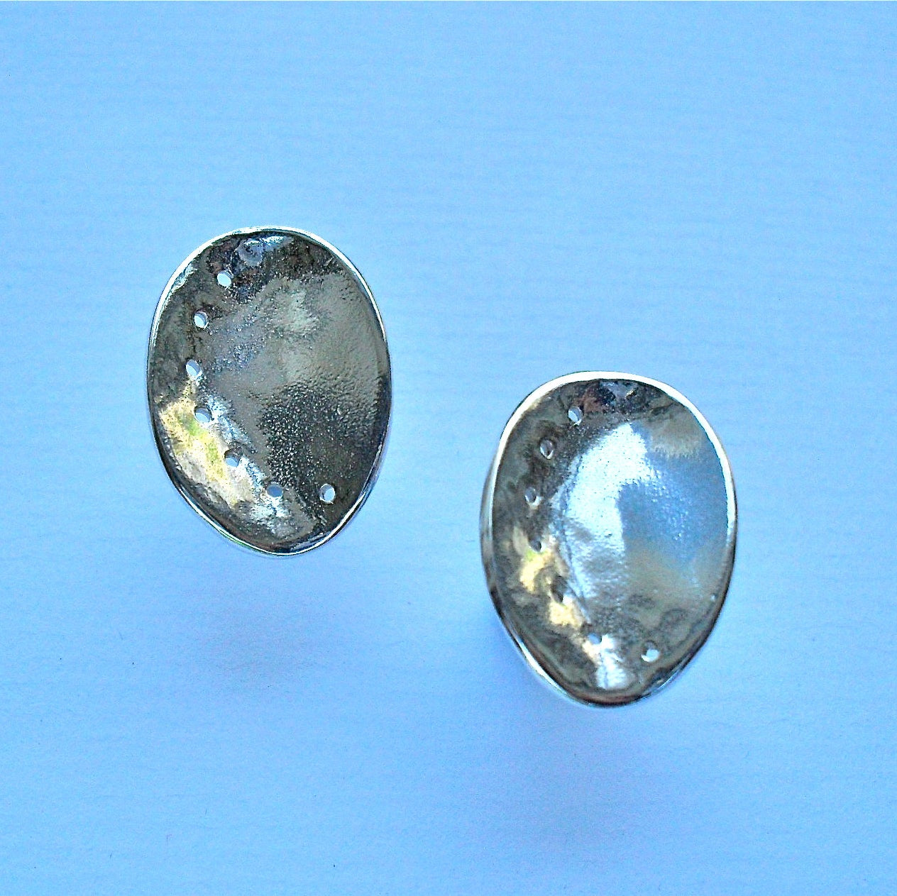 Pair of silver ormer stud earrings on a light blue background