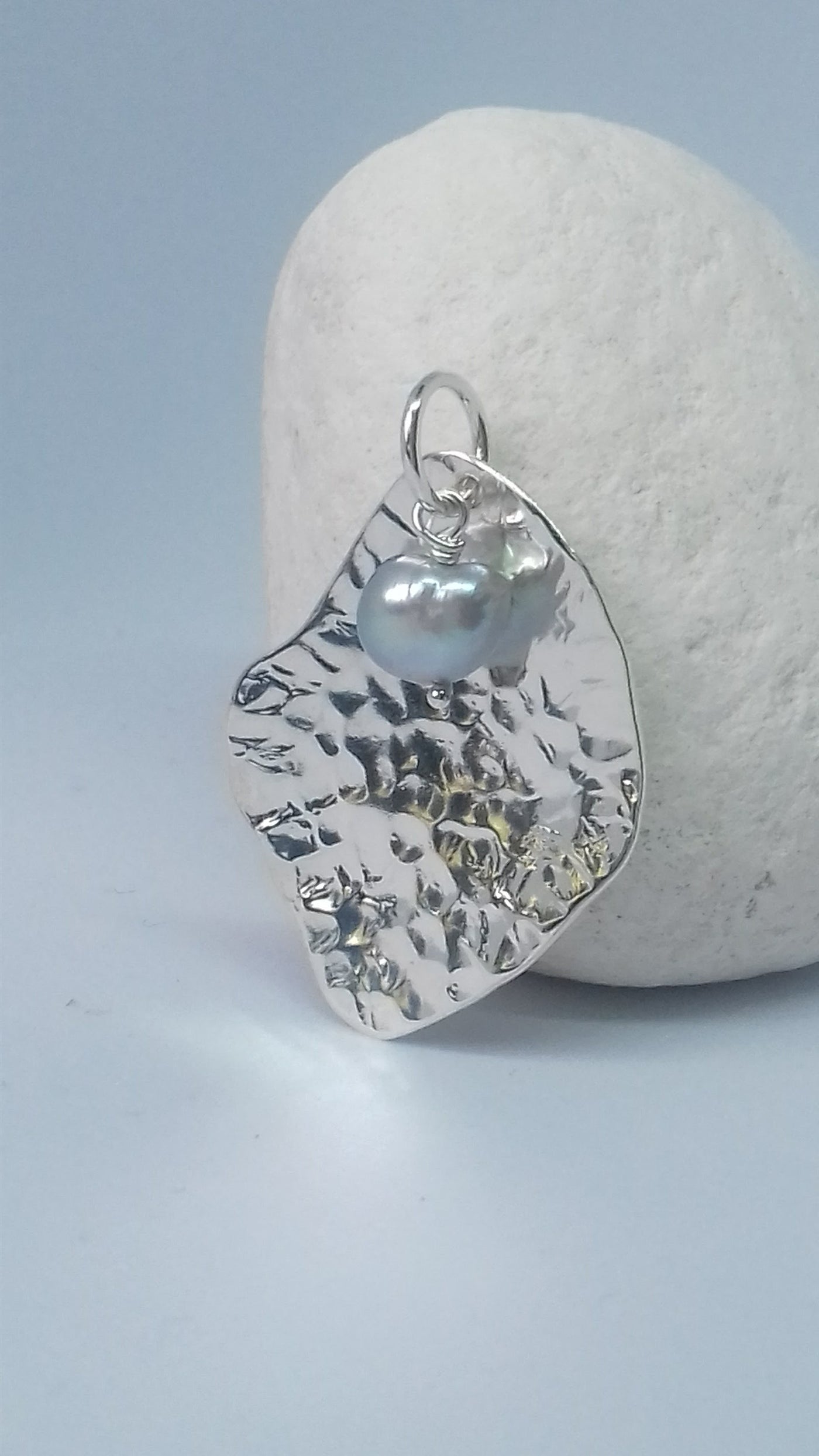 Silver potato peel pendant with a pearl on a stone surface