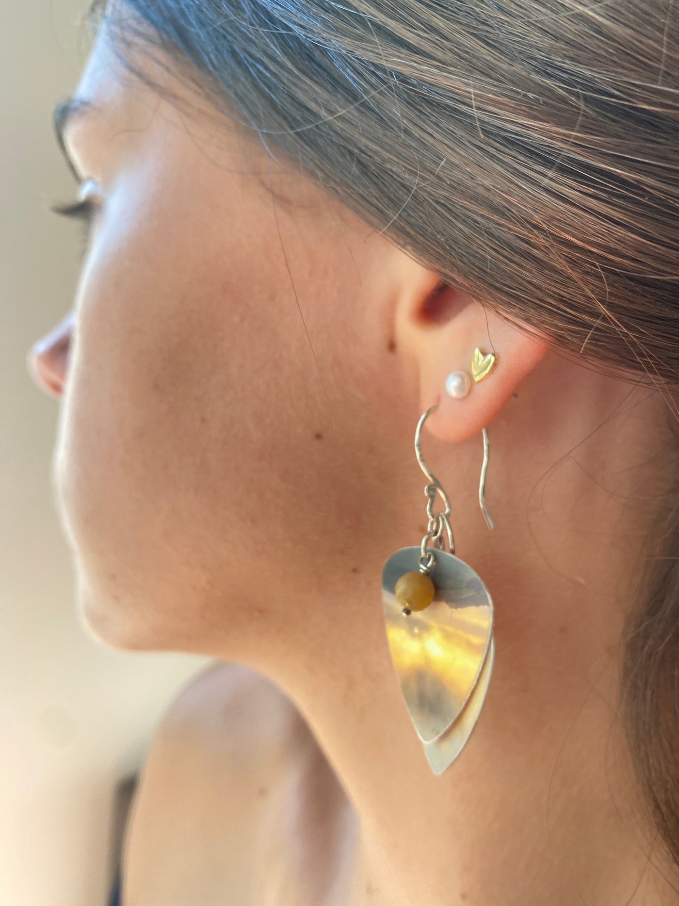 Close-up of a model wearing a silver and recycled plastic layered earring in muted yellows and oranges 