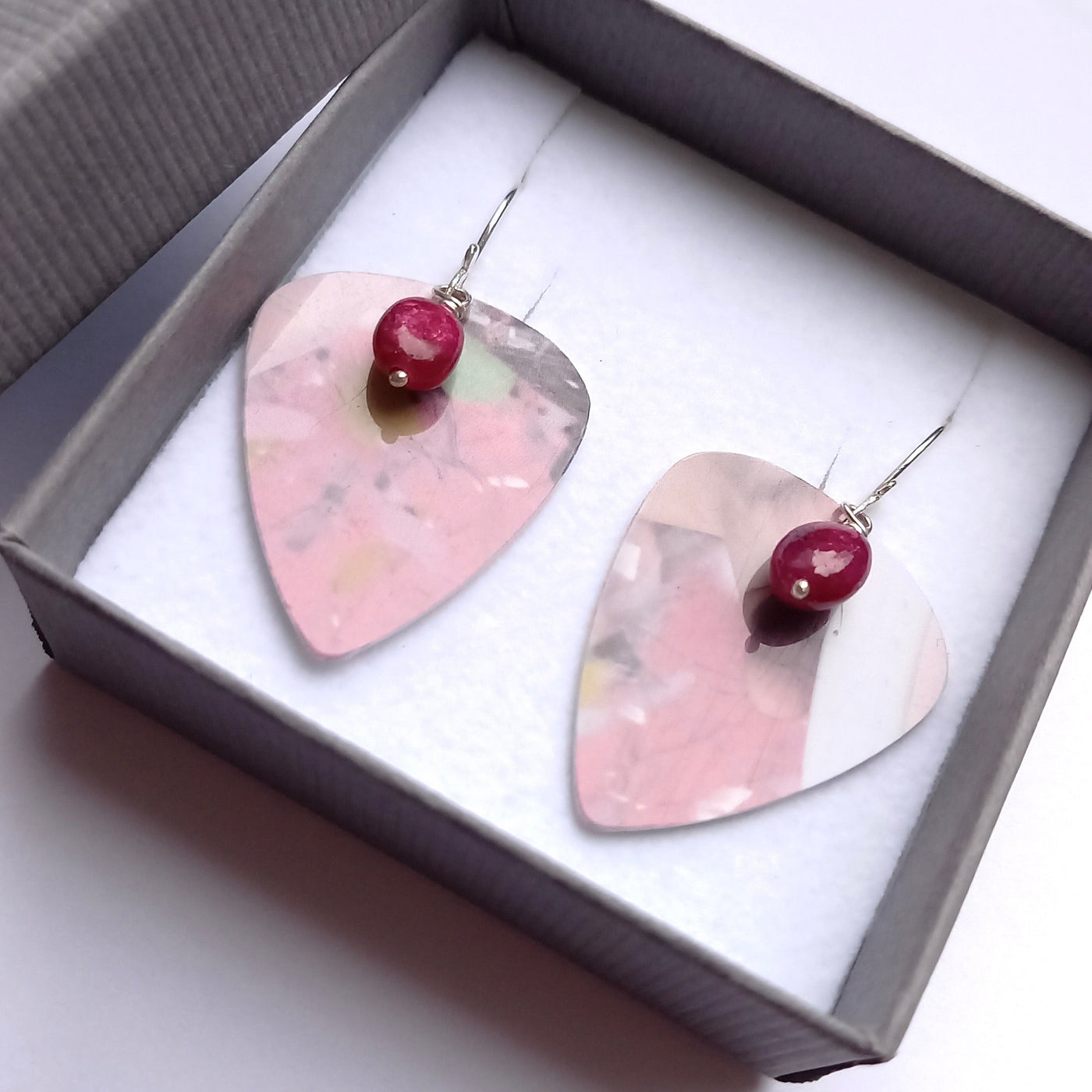 Guitar pick earrings in pink with a ruby gemstone, displayed in a gift box