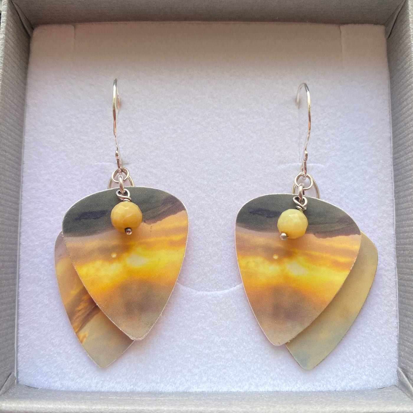 Pair of plectrum shaped earrings with layered yellow and brown design in a box