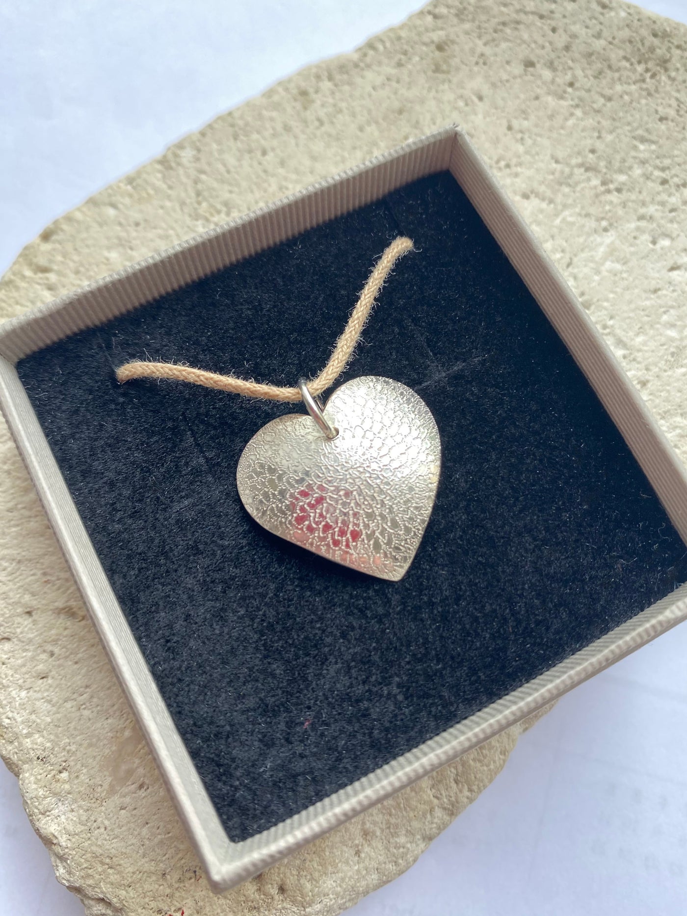 Silver heart-shaped pendant in a box on a textured surface