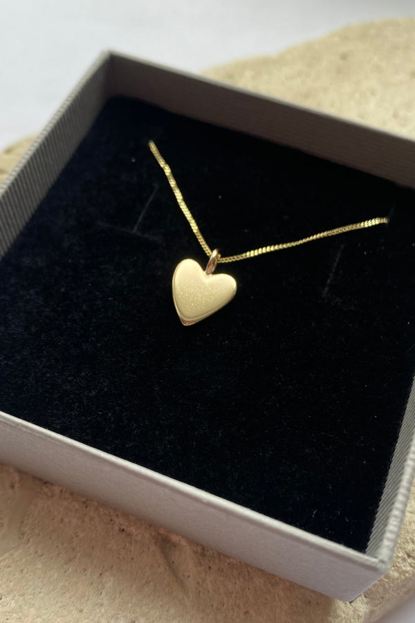 Gold heart-shaped necklace in a black box on a textured surface