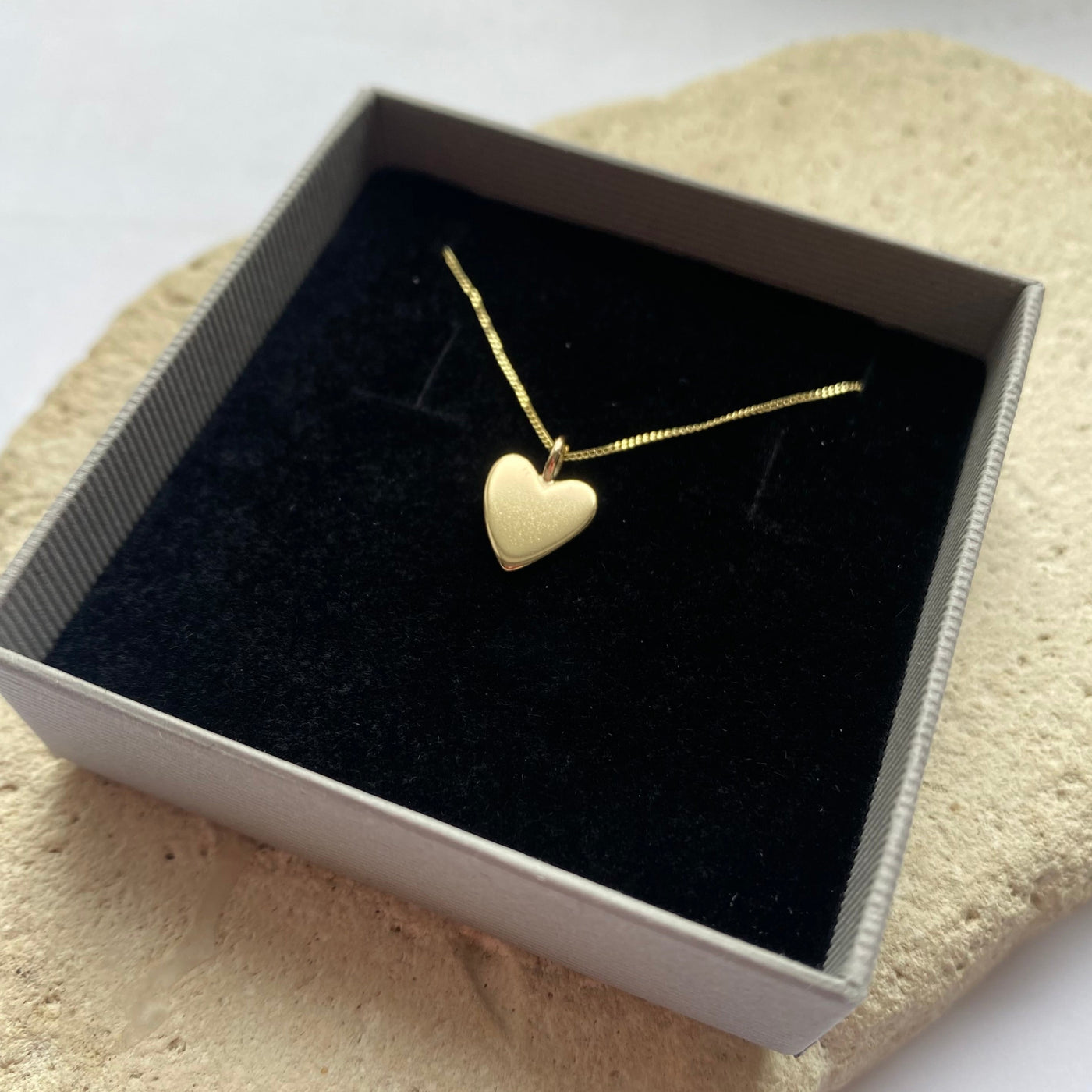 Gold heart-shaped necklace in a black box on a textured surface