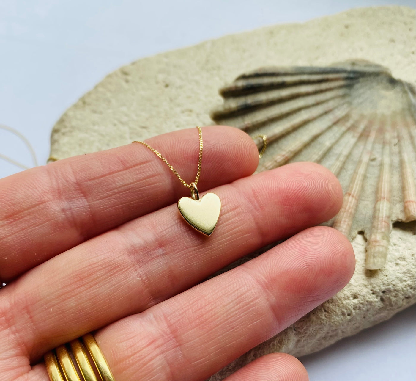Gold heart-shaped pendant on a chain held by a hand with a shell in the background