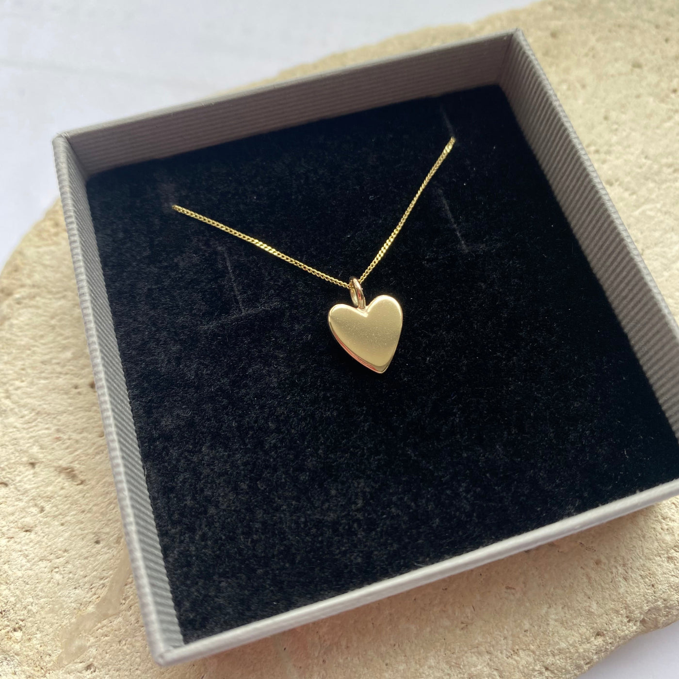 Gold heart-shaped necklace in a box on a textured surface