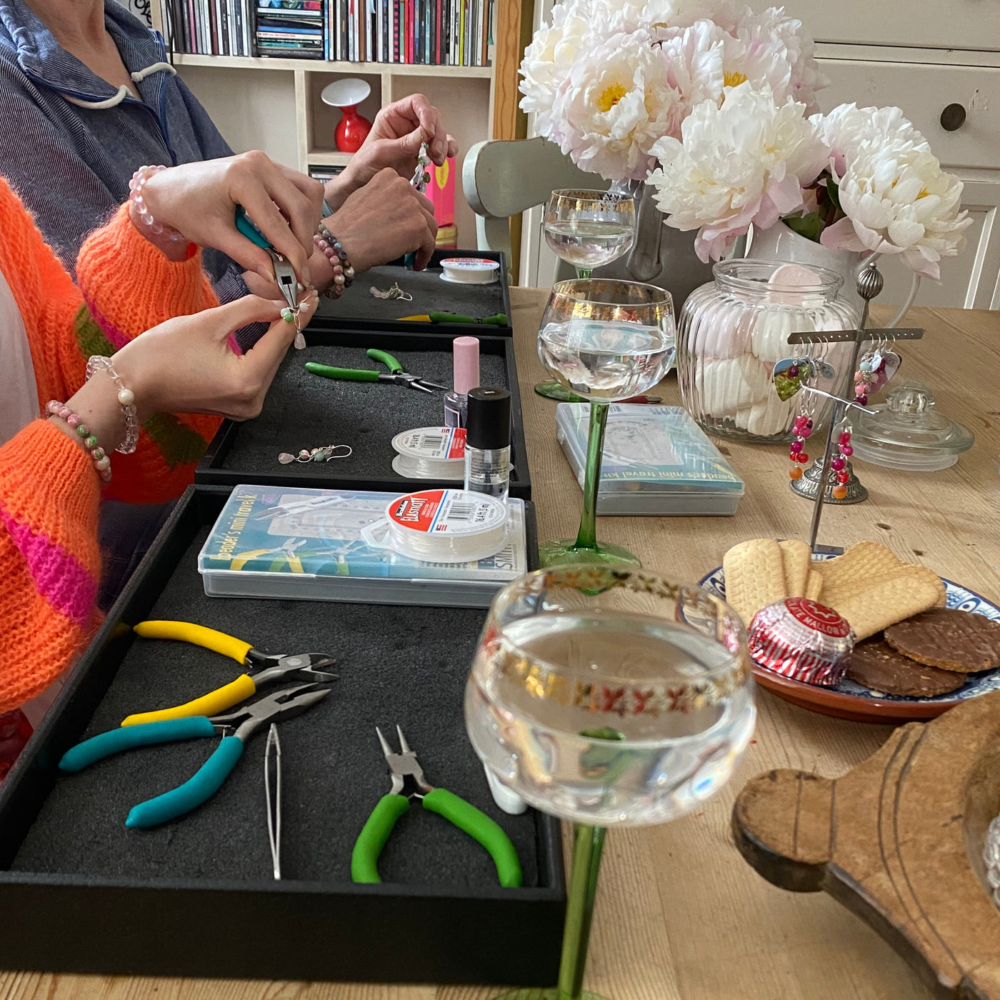 A lifestyle scene of a jewelry-making workshop table with people crafting earrings using pliers. I