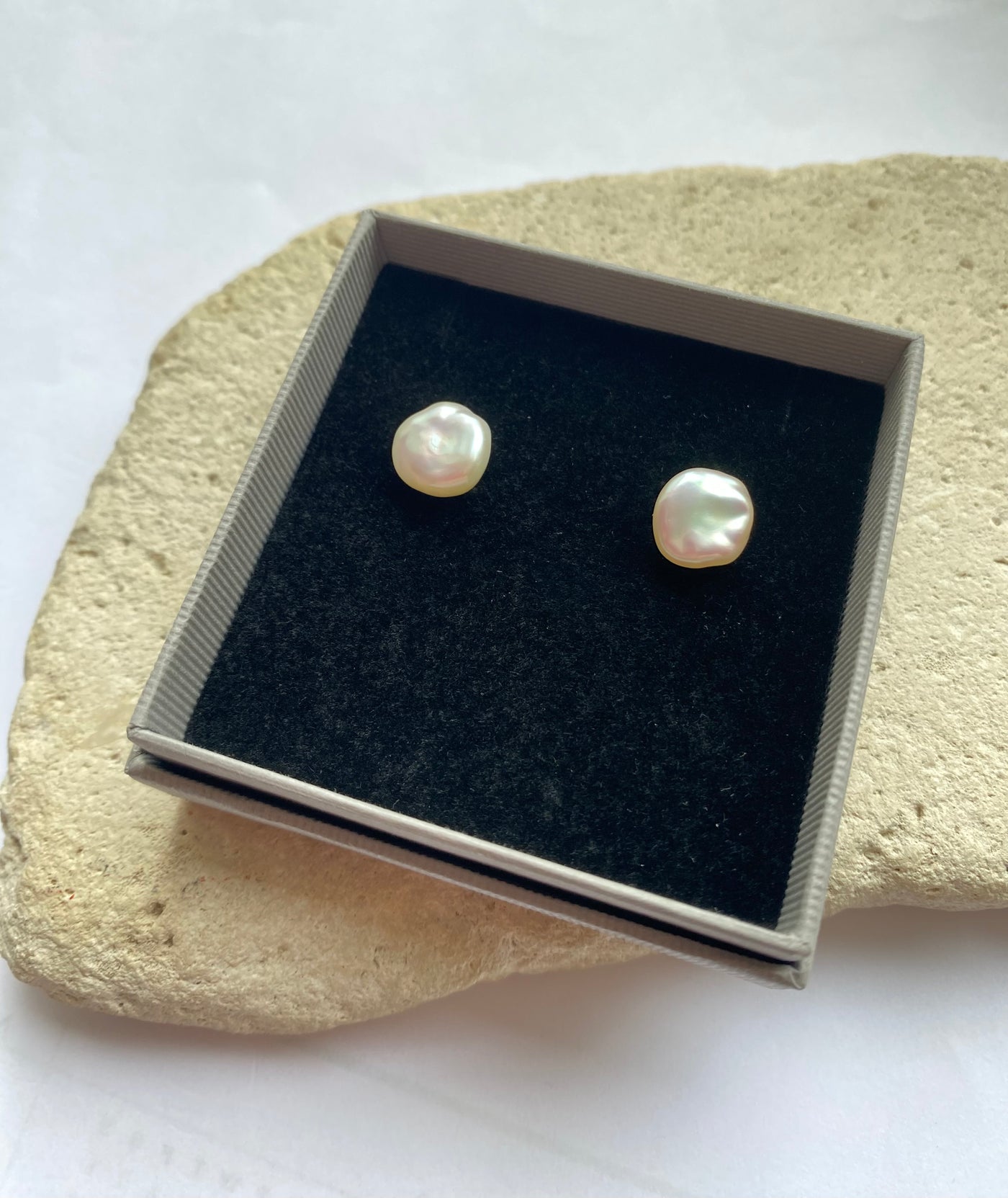 Pearl stud earrings in a jewelry box on a stone surface