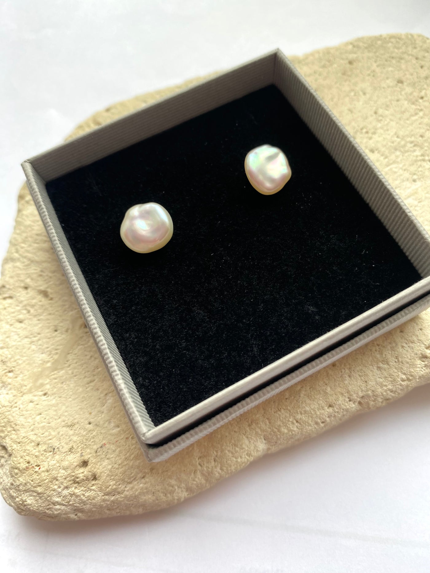 Pair of pearl earrings in a jewelry box on a stone surface