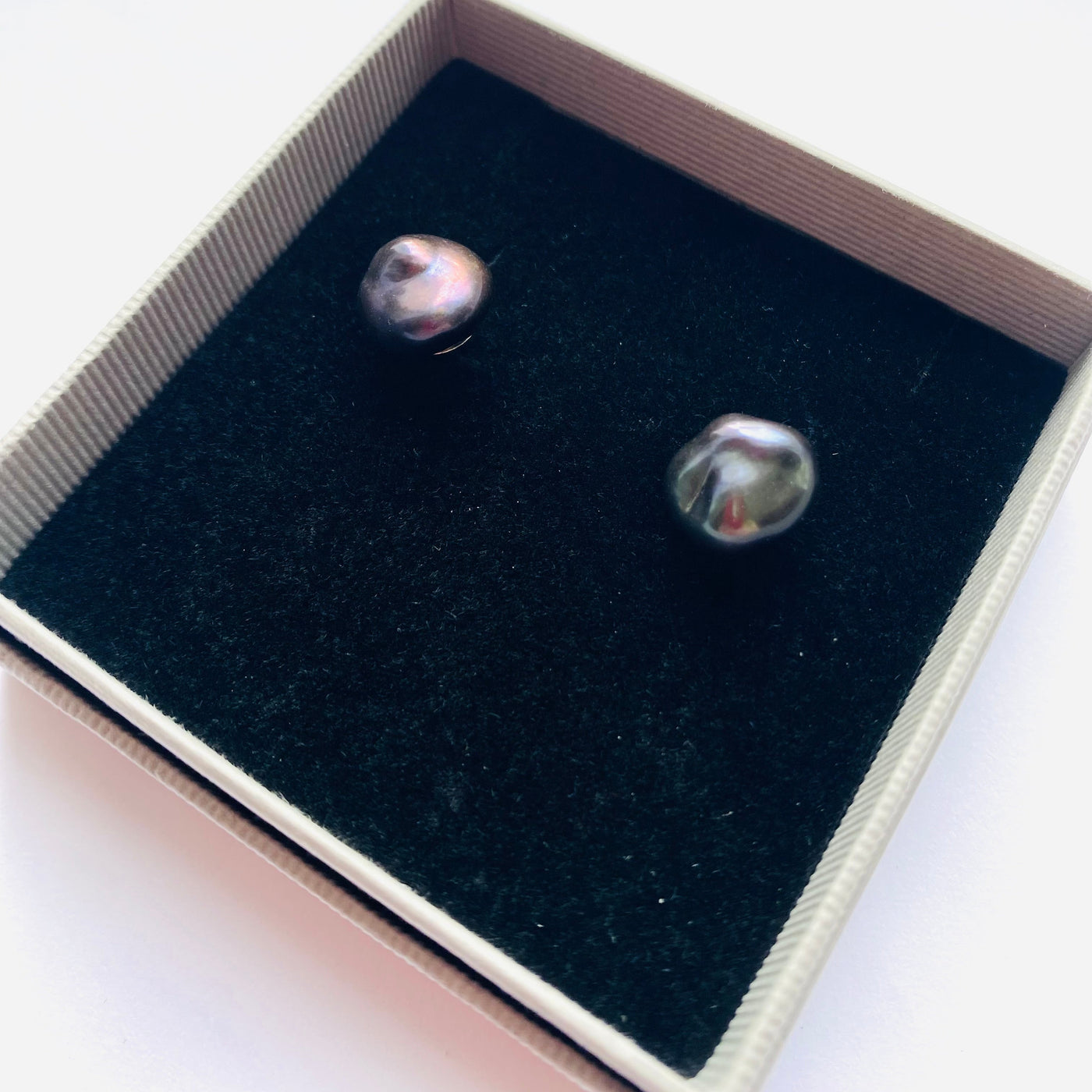 Pair of silver stud earrings with peacock blue baroque freshwater pearls in a black lined jewellery gift box on a white background