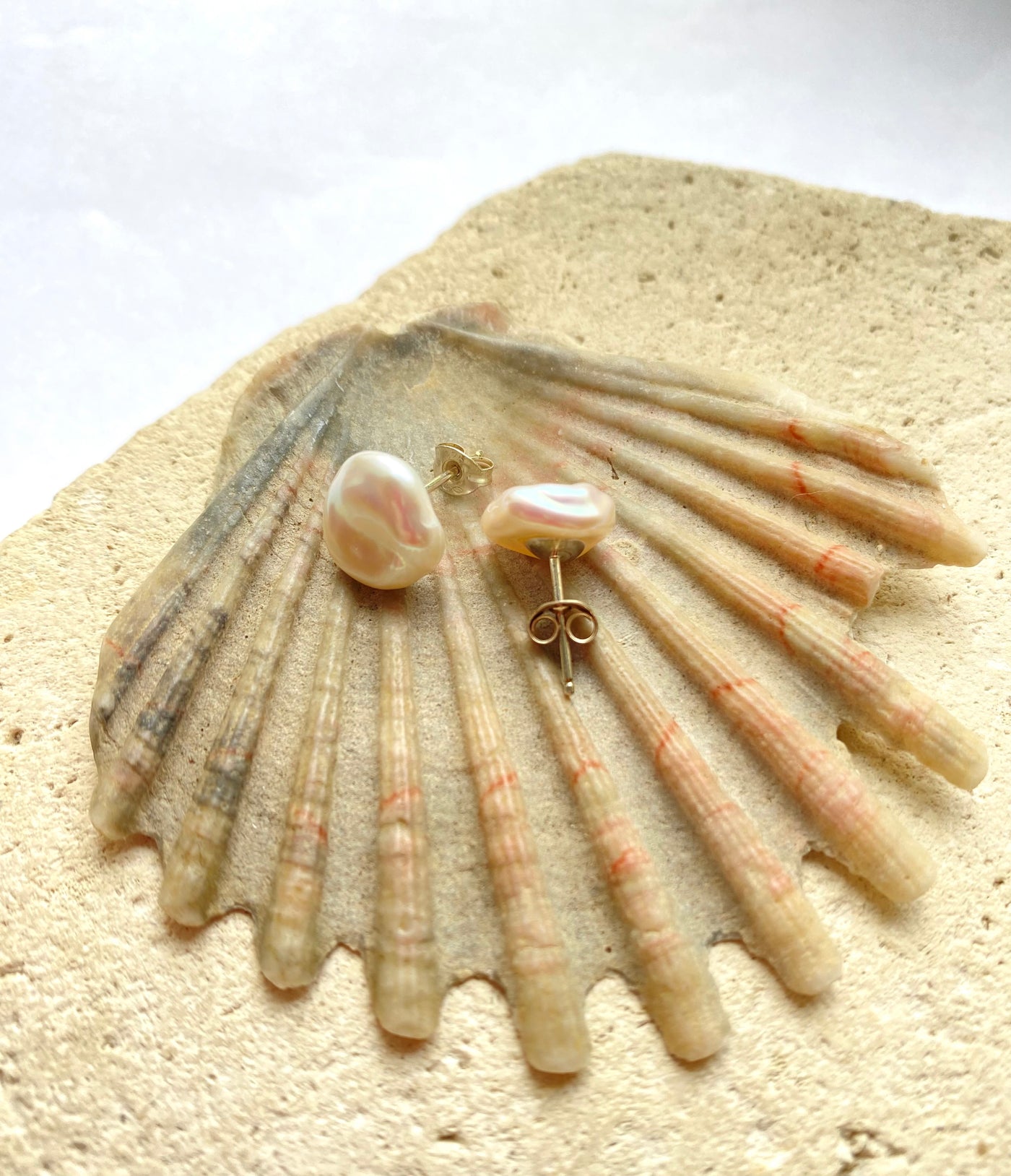 Pair of pearl earrings on a seashell with a white background