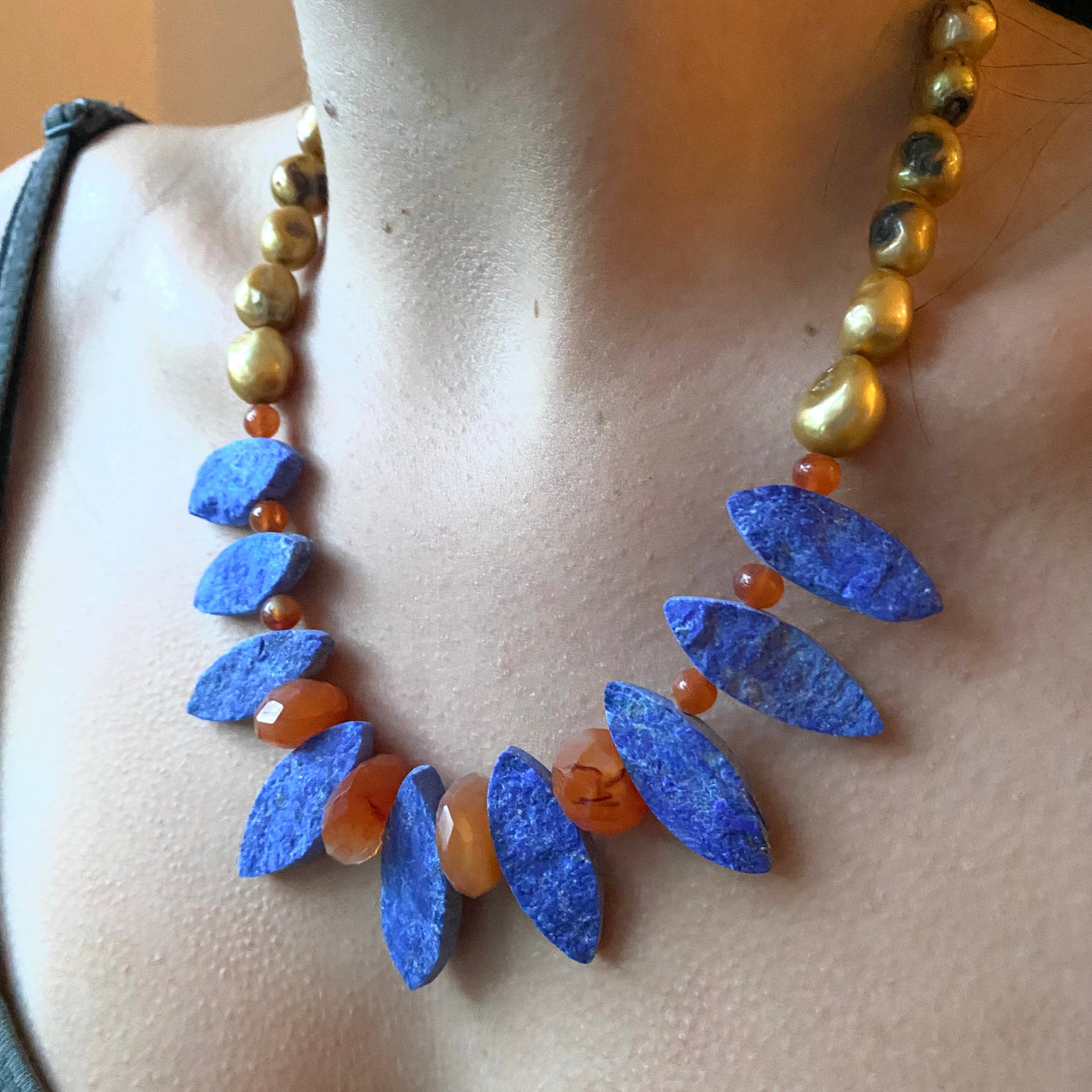 Necklace with blue lapis lazuli gemstones cut into a marquise shape with orange carnelian beads on a model. 