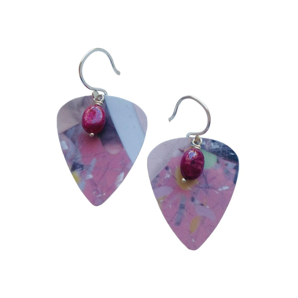 Pair of pink guitar pick earrings with red ruby gemstones on a white background