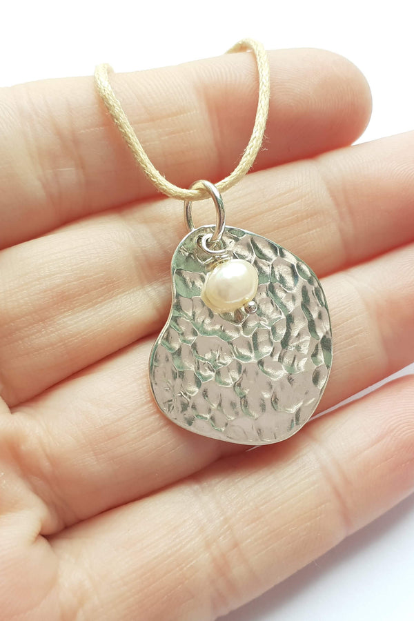 Hand holding a silver pendant necklace with a white background