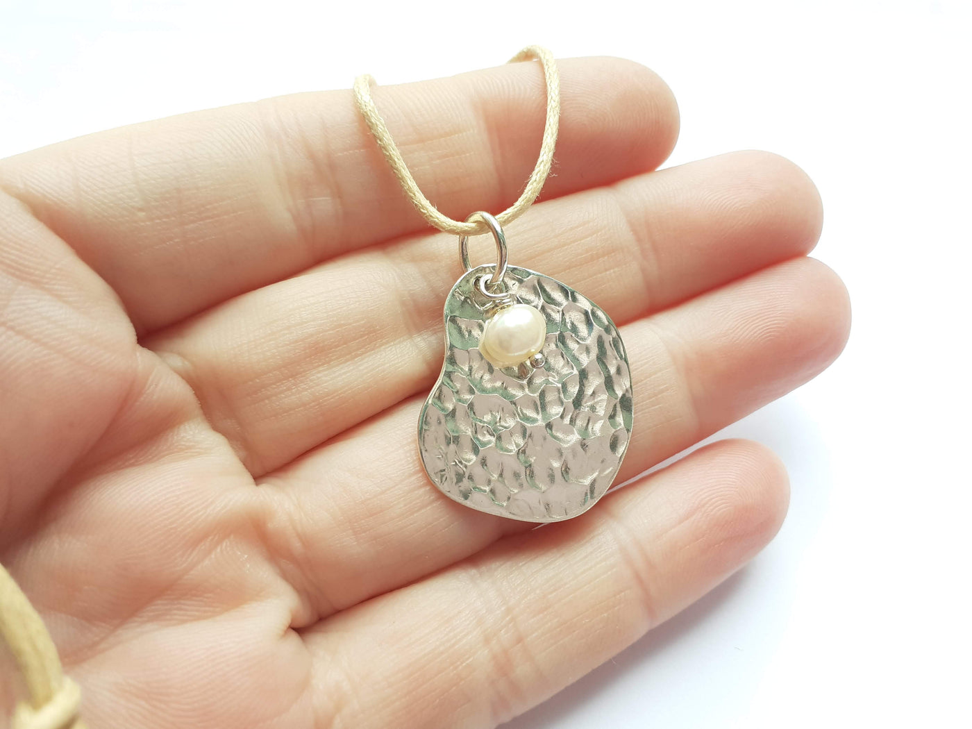 Hand holding a silver pendant necklace with a white background