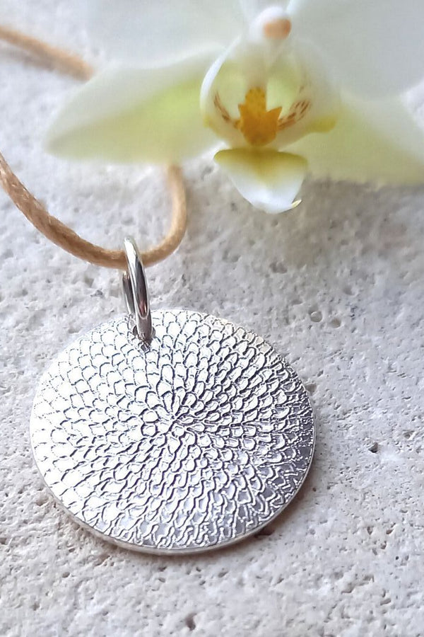 Silver chrysanthemum textured hand engraved disc pendant on a beige cord 
