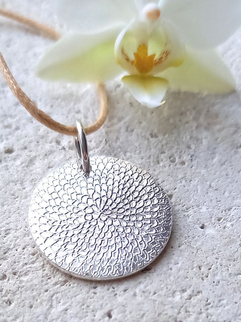 Silver chrysanthemum textured hand engraved disc pendant on a beige cord 
