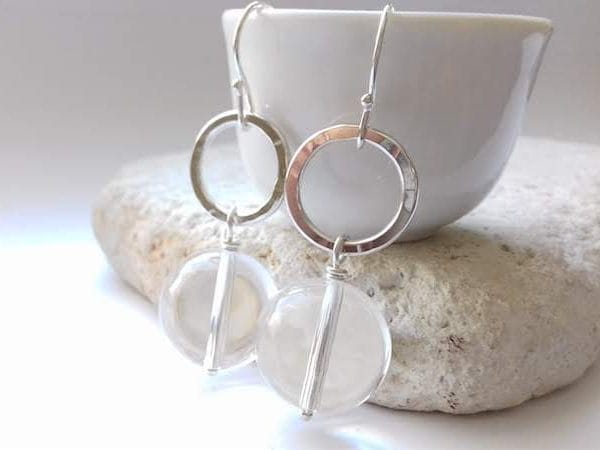 Silver hoop earrings with clear circular pendants in clear quartz rock crystal gemstone on a white background