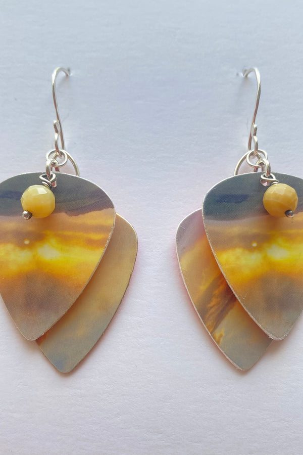 Guitar pick-shaped earrings with a yellow bead on a white background