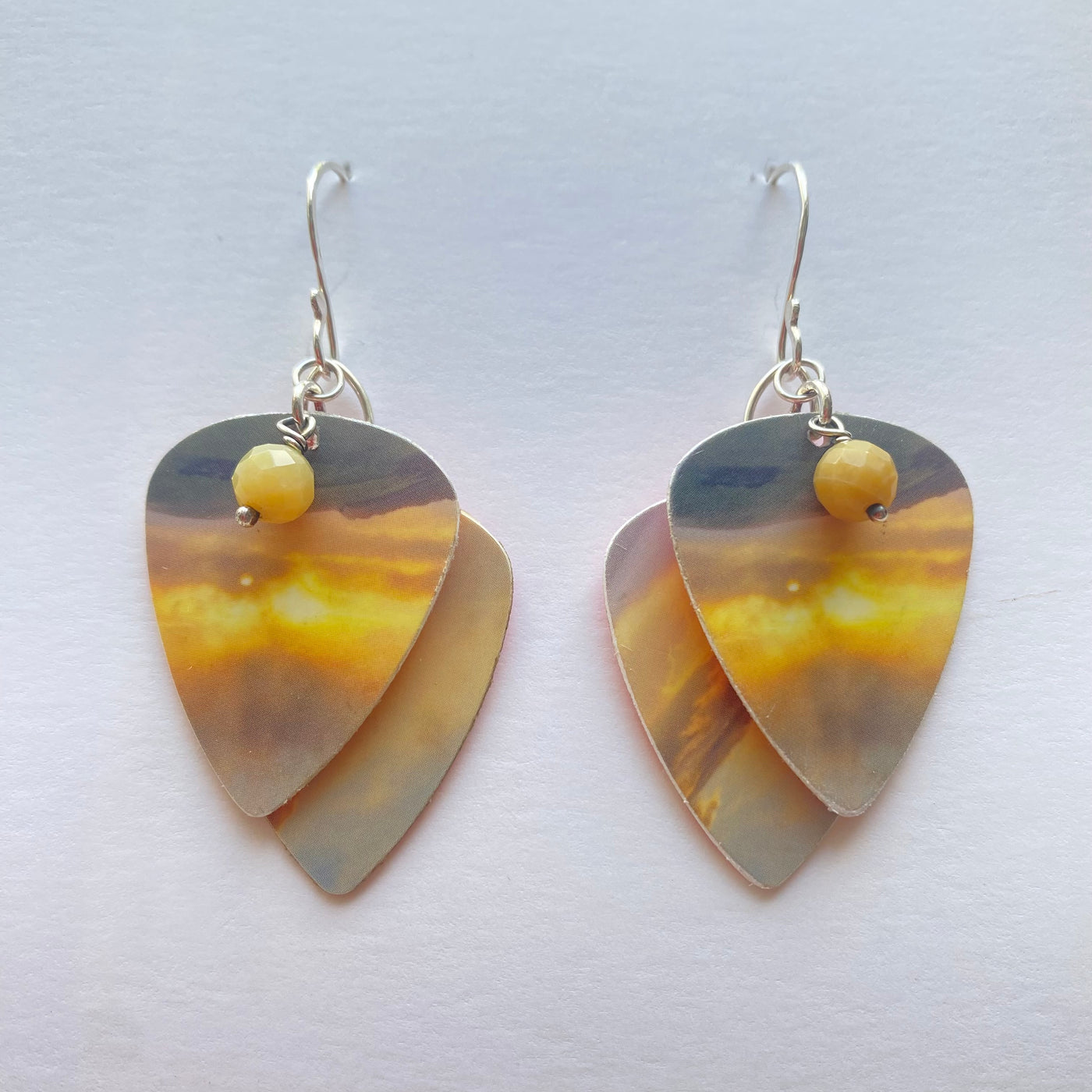 Guitar pick-shaped earrings with a yellow bead on a white background
