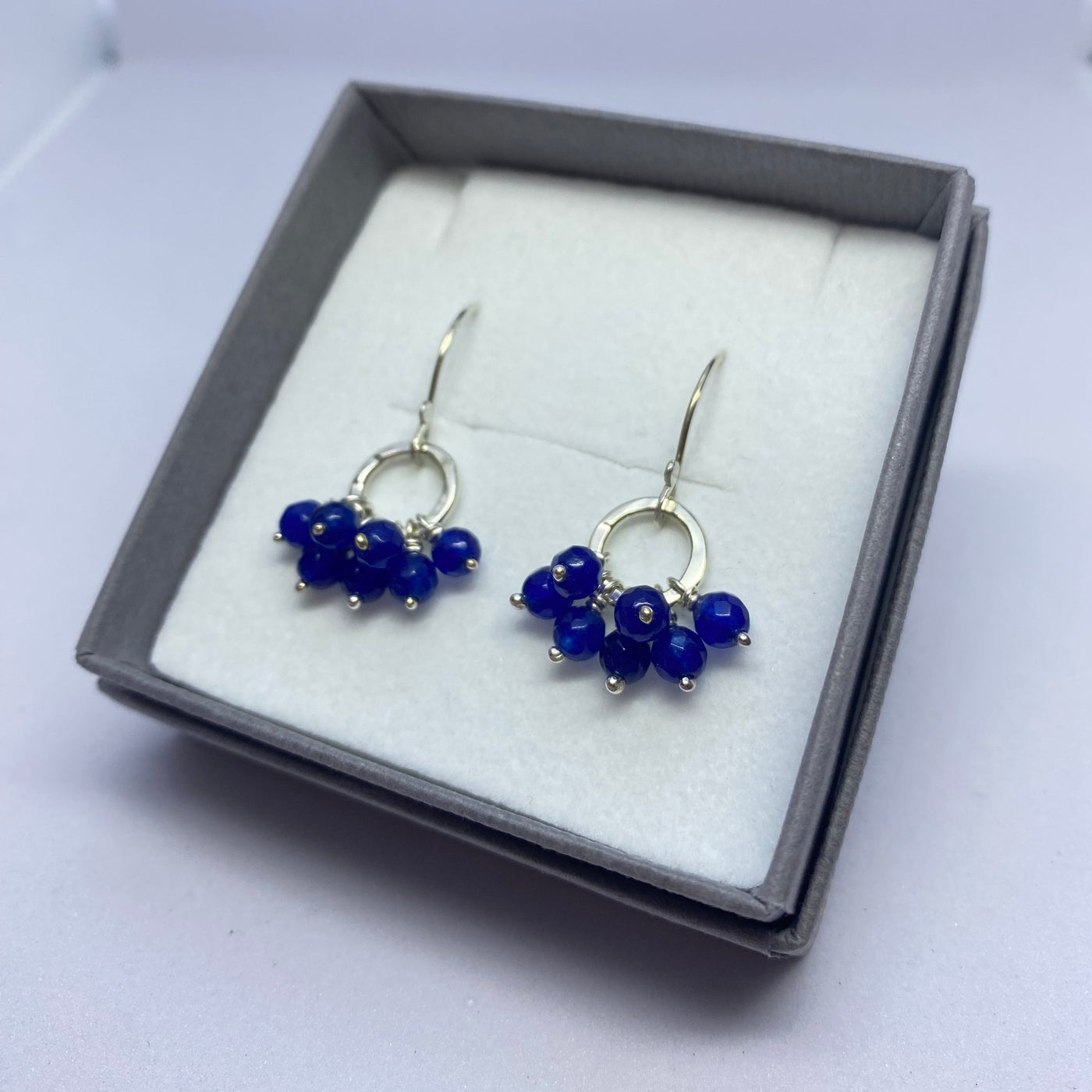 Pair of blue beaded earrings in a gray box on a white background