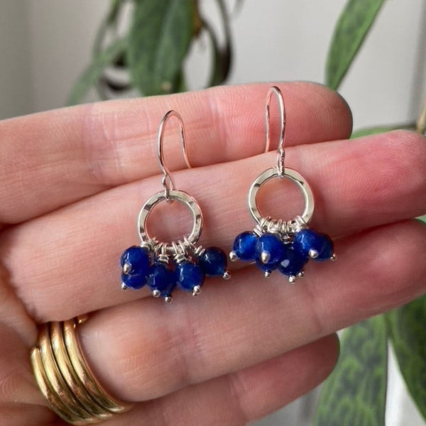 Blue sapphire ruffle disco circle earrings, held on a hand