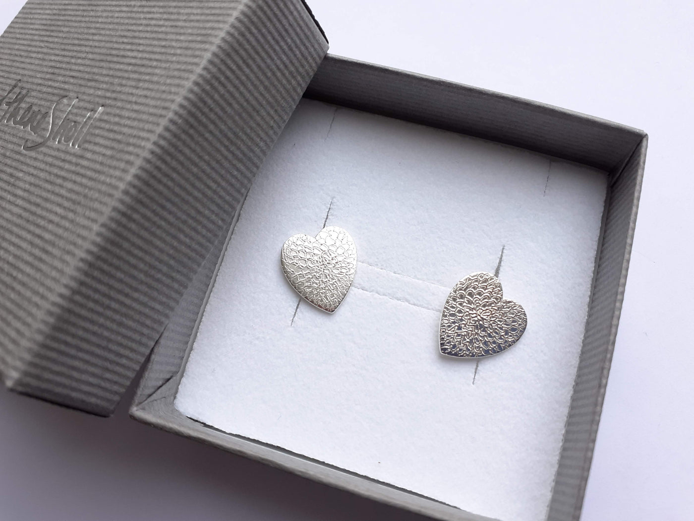 Heart-shaped silver earrings in a branded box on a light background