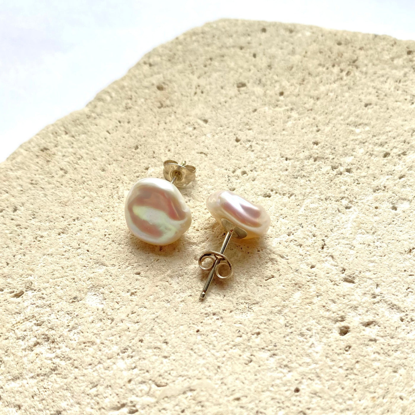 Pair of pearl stud earrings on a textured beige surface