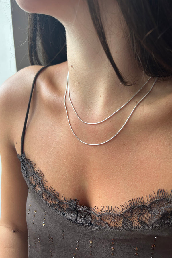 Close-up of a person wearing two silver snake chains to illustrate how the different lengths sit on the body. 