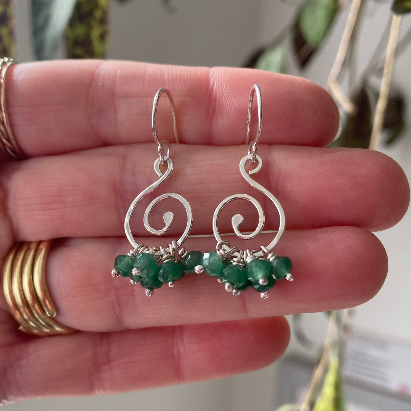 spiral earrings in silver with a ruffle of emerald gemstones hanging from the base of the spiral, held on the hand that made them