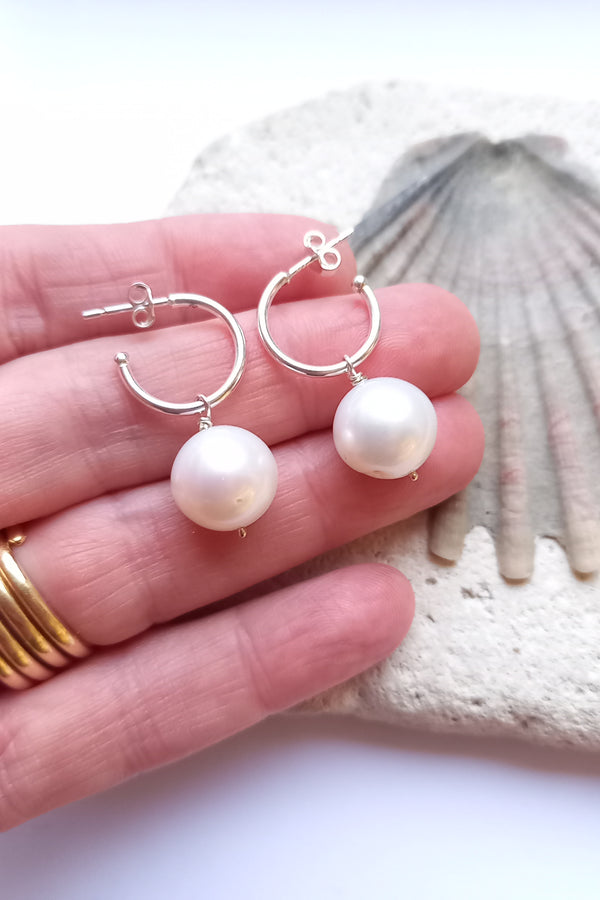Pearl earrings held in a hand with a shell in the background