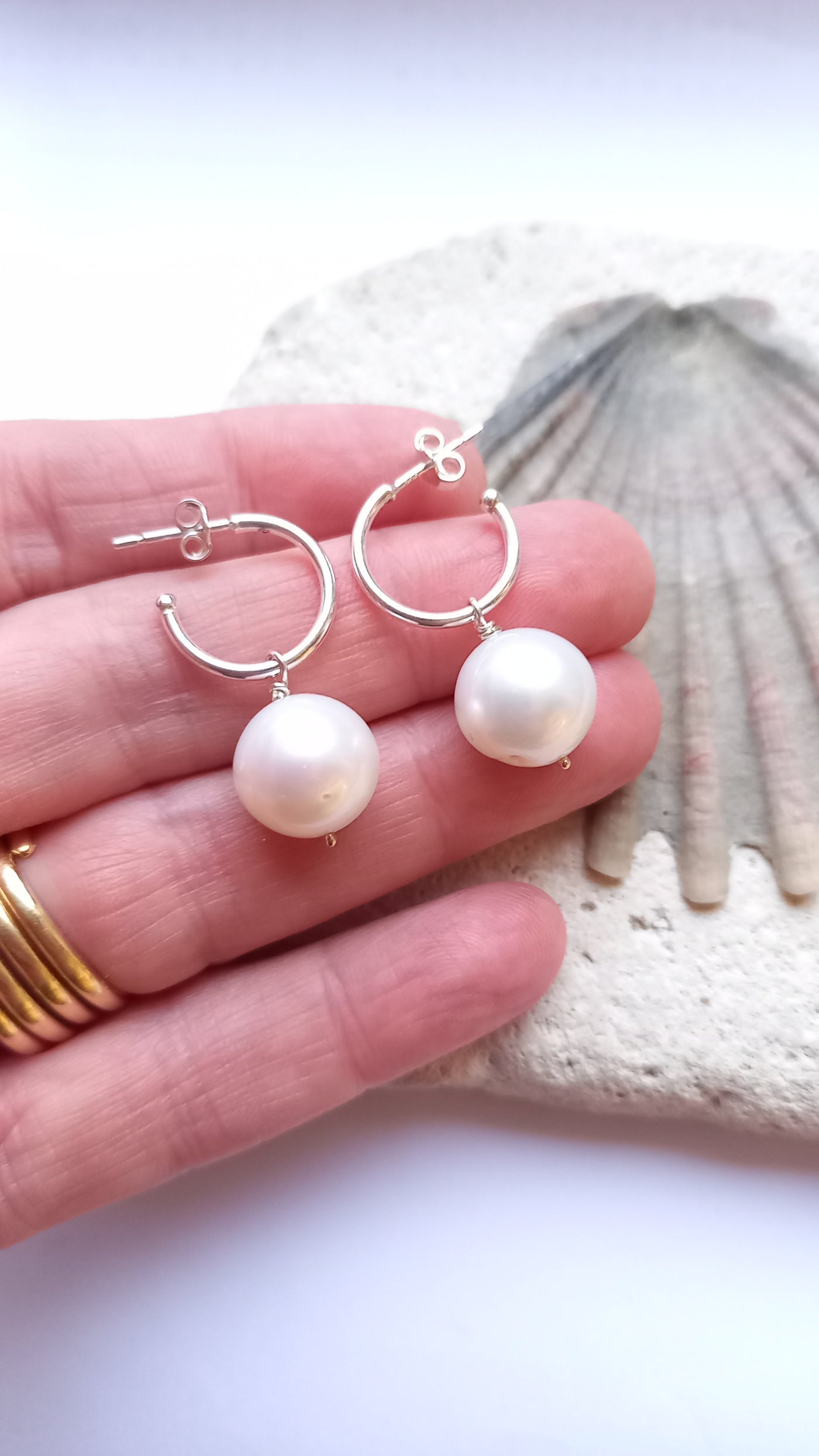 Pearl earrings held in a hand with a shell in the background