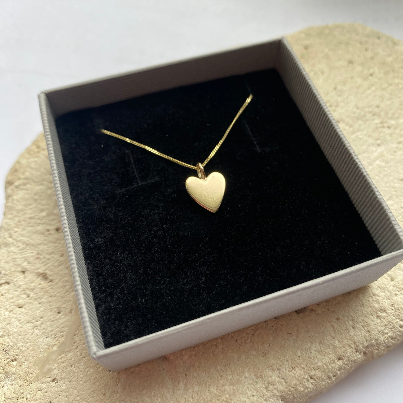 Gold heart necklace in a box on a textured surface
