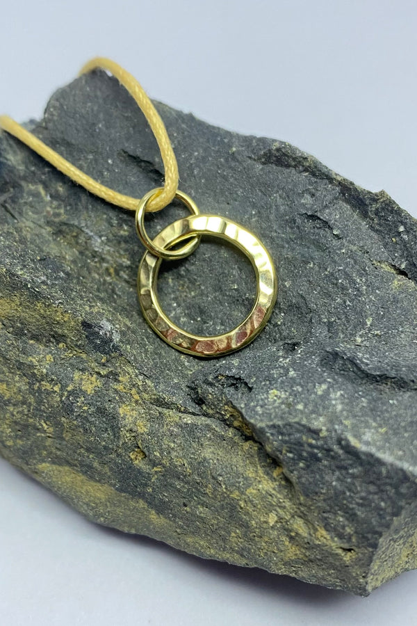  Circular pendant in a textured finish in bright yellow 9ct gold on a piece of dark stone.
