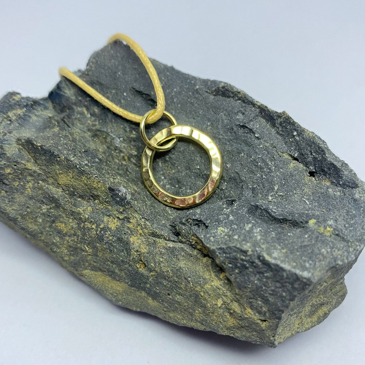  Circular pendant in a textured finish in bright yellow 9ct gold on a piece of dark stone.
