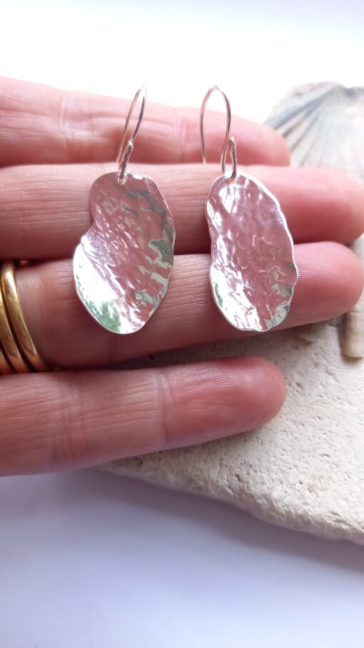 Abstract textured sterling silver earrings laying between the first finger and ring finger on a hand
