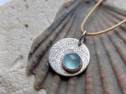 silver circle pendant with engraved petal design spiraling towards a set smooth aquamarine stone at the bottom right of the pendant