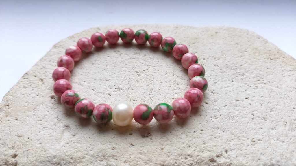 Smooth round beaded bracelet made from pink and green marbled beads with larger pearl accent