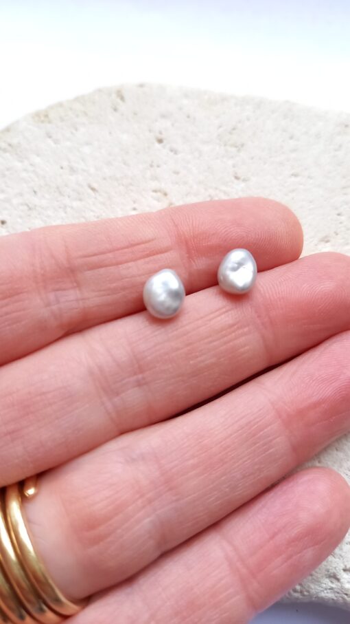 Pair of light grey wonky pearl studs on hand