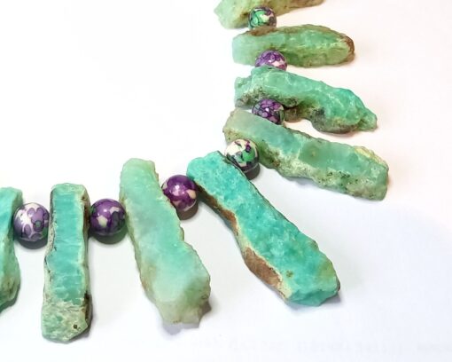 Close up of Long green gemstone slabs alternating with smooth purple and green spotty beads