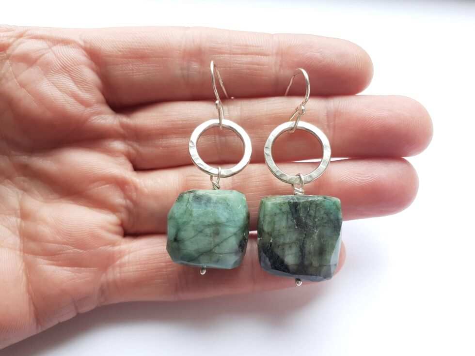 Emerald and silver circle earrings hanging on a hand